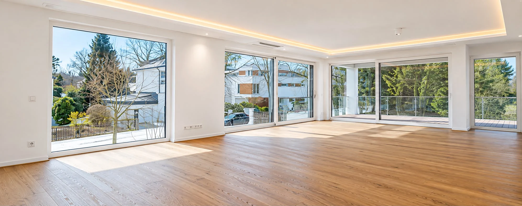 Bright living space with a wooden floor, large windows and indirect ceiling lighting
